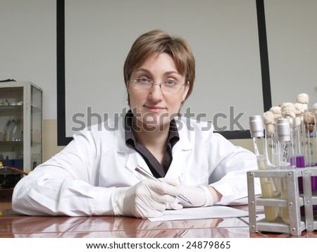 Portrait of female laboratory technician sitting behind laboratory desk with test tubes
