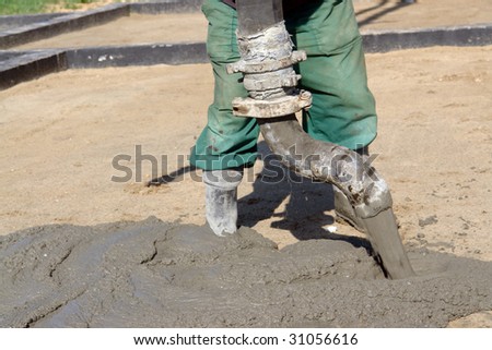 Closeup of construction worker pouring concrete mix from pump onto compacted foundation surface
