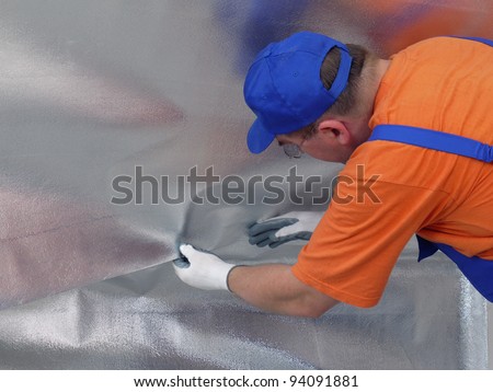 Construction worker affixing vapour insulation foil under thermally insulated attic surface