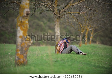 tied man sitting under tree with blue ribbon on eyes