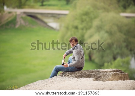 young man sitting on stone with wine bottle
