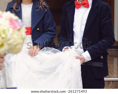 girl with red belt and bow with red bow holding bride\'s veil