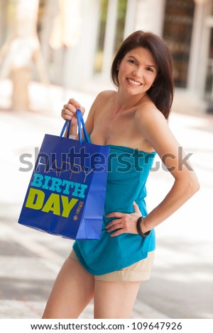 Beautiful woman outdoors in a shopping mall holding a happy birthday bag.