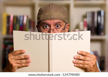 Handsome middle age man reading a book with a bookcase background.