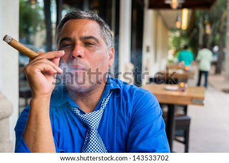 Handsome middle age Hispanic man smoking a cigar outdoors in a restaurant.