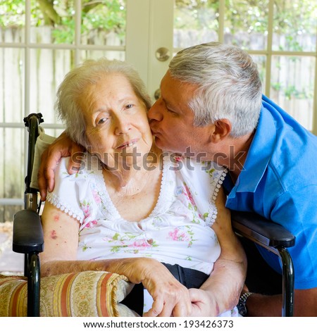 Elderly eighty plus year old woman in a wheel chair in a home setting with her son.