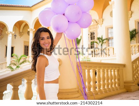Beautiful young woman in a outdoor courtyard setting holding balloons.