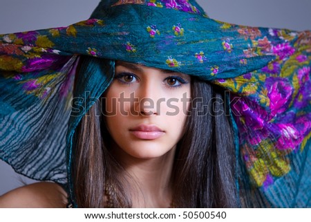 Beautiful and exotic young woman of multiple ethnicity wearing a blue/purple veil spread over her head.