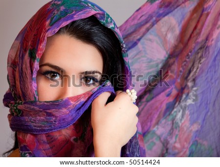 Beautiful young woman of multiple ethnicity in a glamour/fashion pose with a shawl partially covering her face on a gray background.