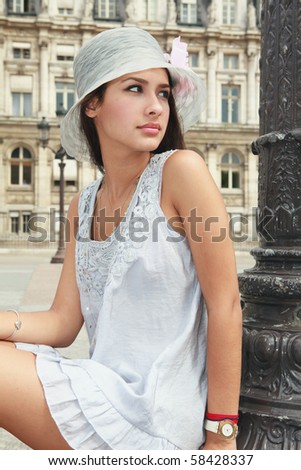 Beautiful young woman in a fashion pose in a plaza in Paris, France with historical building in the background .