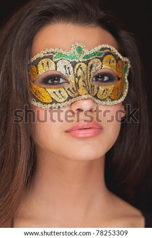 Beautiful exotic young yoman wearing a masquerade mask against a black background.