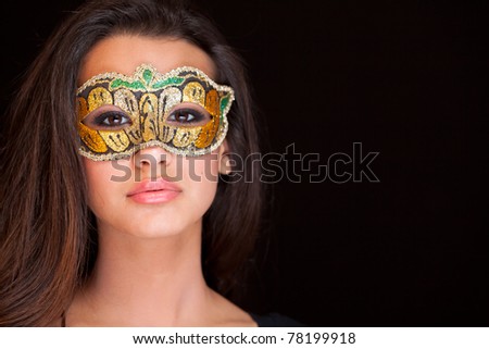 Beautiful exotic young woman wearing a masquerade mask against a black background.