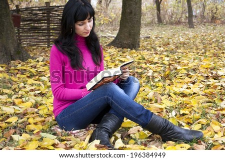 The beautiful woman reads the book in an autumn garden