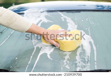The process of cleaning the windows of the car using shampoo and yellow sponges in the yard