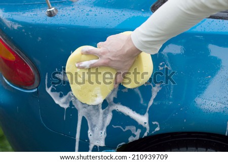 The process of washing a blue car with the help of shampoo and yellow sponges in the yard