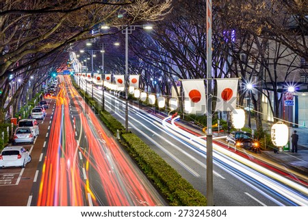 Harajuku, Tokyo, Japan traffic flows below Japanese flags at night.