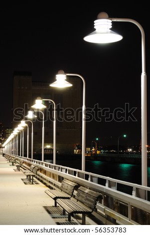 Benches and lamp posts on a pier at night.