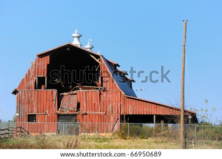 An old barn with a collapsed wall across an empty field