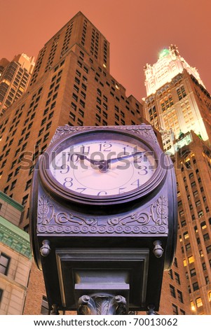 An old fashion clock in downtown Manhattan with skyscrapers behind it.