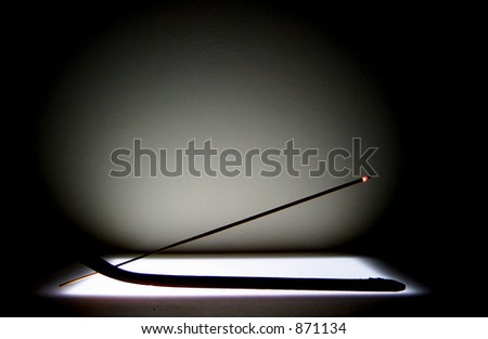 lit incense stick in holder, lit and glowing. On light box, glowing white circular background