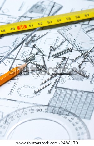 Nails, pencil, tape measure and geomteric tools on top of floor plan. Focus on the tip of pencil and nails.
