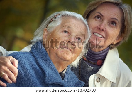 Elderly woman and her middle-aged daughter looking above. Focus on the elderly woman.