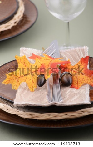 Autumn theme place setting with brown plates and colorful fabric leaves on pale green background