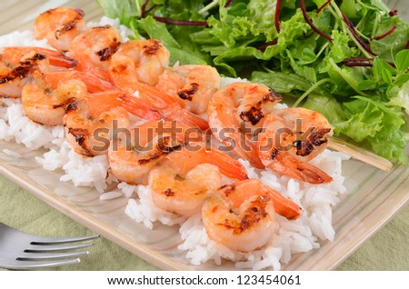 Spicy barbecued prawn skewers on a bed of white rice and salad greens
