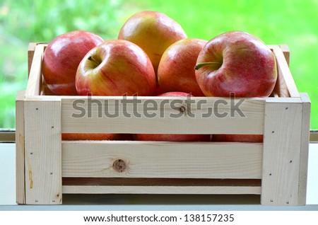 Delicious Gala apples in wooden crate on windowsill with vibrant green background