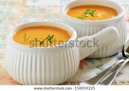 Creamy carrot and sweet potato soup with sprig of thyme in white ribbed soup bowls