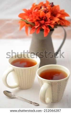 Two mugs of hot tea with vibrant Fall flower arrangement in rustic jug in vertical format