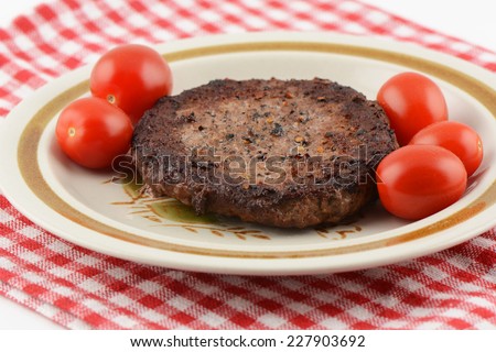 Freshly grilled lean hamburger patty with sea salt and coarse black pepper, cherry tomatoes on red and white cloth in horizontal format