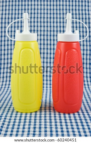Mustard and ketchup bottles on blue and white check cloth in vertical format