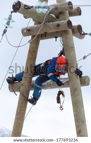 electrician working on top of an electricity pylon with the use of claws-manholes and belt