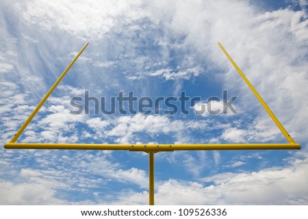 Yellow American football metal field goal against a partially cloudy sky. Viewed from below and the back of the field goal.