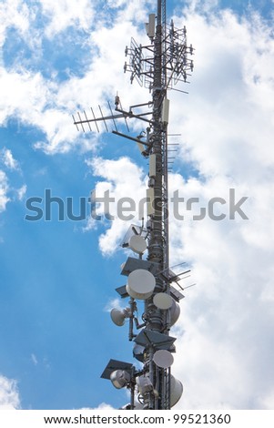 Electronic communications and cell phone tower under partially cloudy sky. Vertical format.