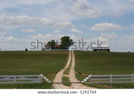 A farm on a hill in Central Texas. White wooden fence around. Curvy unpaved road leads to the house.