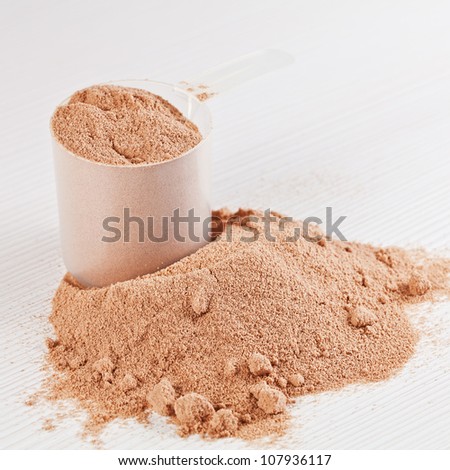 Scoop of chocolate whey isolate protein powder or weight loss powder spilling out of a measuring scoop on white wooden board