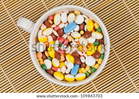Top view of white cup filled with white, red, green, brown, blue and yellow medicine pills and capsules served as breakfast