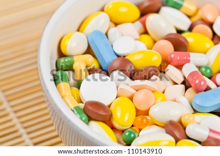 White bowl filled with white, red, green, brown, blue and yellow medicine pills and capsules served as breakfast