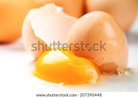Broken egg with yolk and egg white on white board, with egg shells and whole eggs in the background