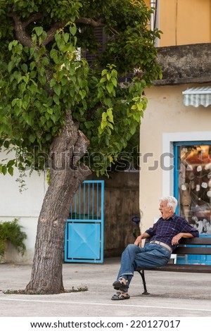VELI IZ, CROATIA - AUGUST 19, 2014: Male senior citizens sitting on the bench under the tree in Veli Iz on island Iz, in front of the shop. Veli Iz is largest settlement on the island Iz.