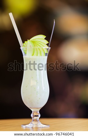 Apple smoothie in a hurricane glass with straw and fresh apple slices on dark background and wooden table