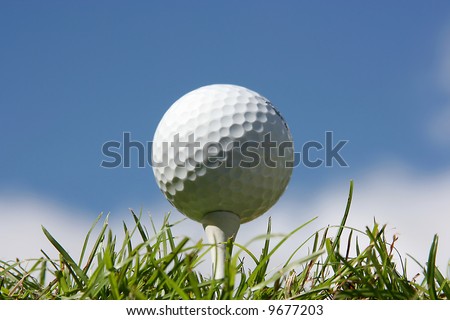 Golf ball on grass against a blue sky and white clouds