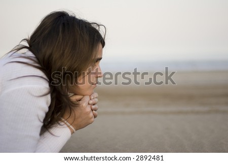 Young woman lying down on the beach with a thoughtful pose (profile)