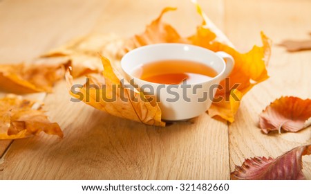 A cup of tea with falling autumn leaves of maple, and a berries of rowan on the background of the wood table