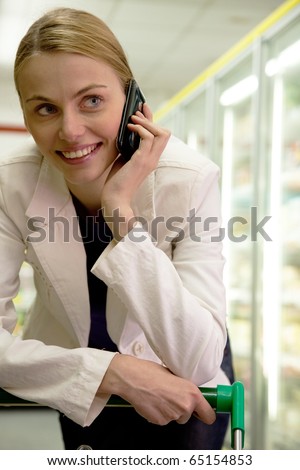 young woman on cell phone with shopping cart in supermarket