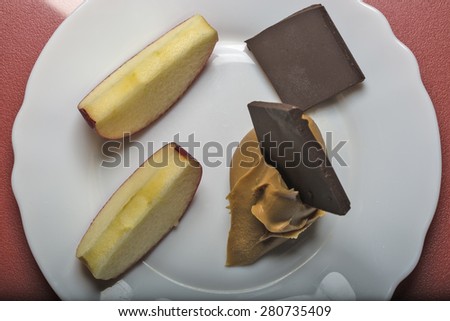 Two apple slices, a dab of peanut butter and pieces of swiss chocolate on a white saucer