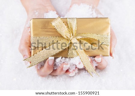 Woman is holding a golden christmas present in her hands - coupon for nail care