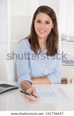 Successful business: young woman in blue blouse sitting at desk smiling and holding pen
